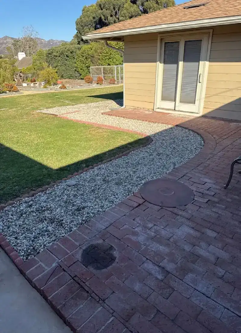 Noncombustible gravel and brick hardscape replacing vegetation around a home foundation