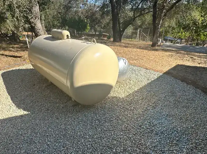 Propane tank placed on noncombustible gravel pad with proper clearance from structure